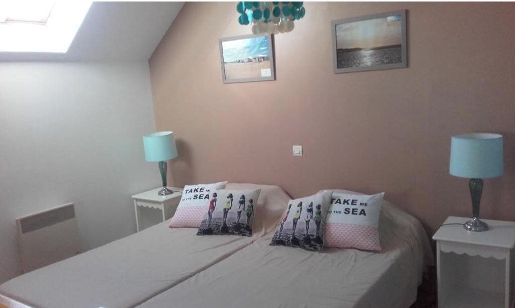 Une chambre à coucher comprenant un lit, deux tables de chevet, deux lampes, deux coussins sur le thème de la plage et deux tableaux encadrés accrochés au mur.