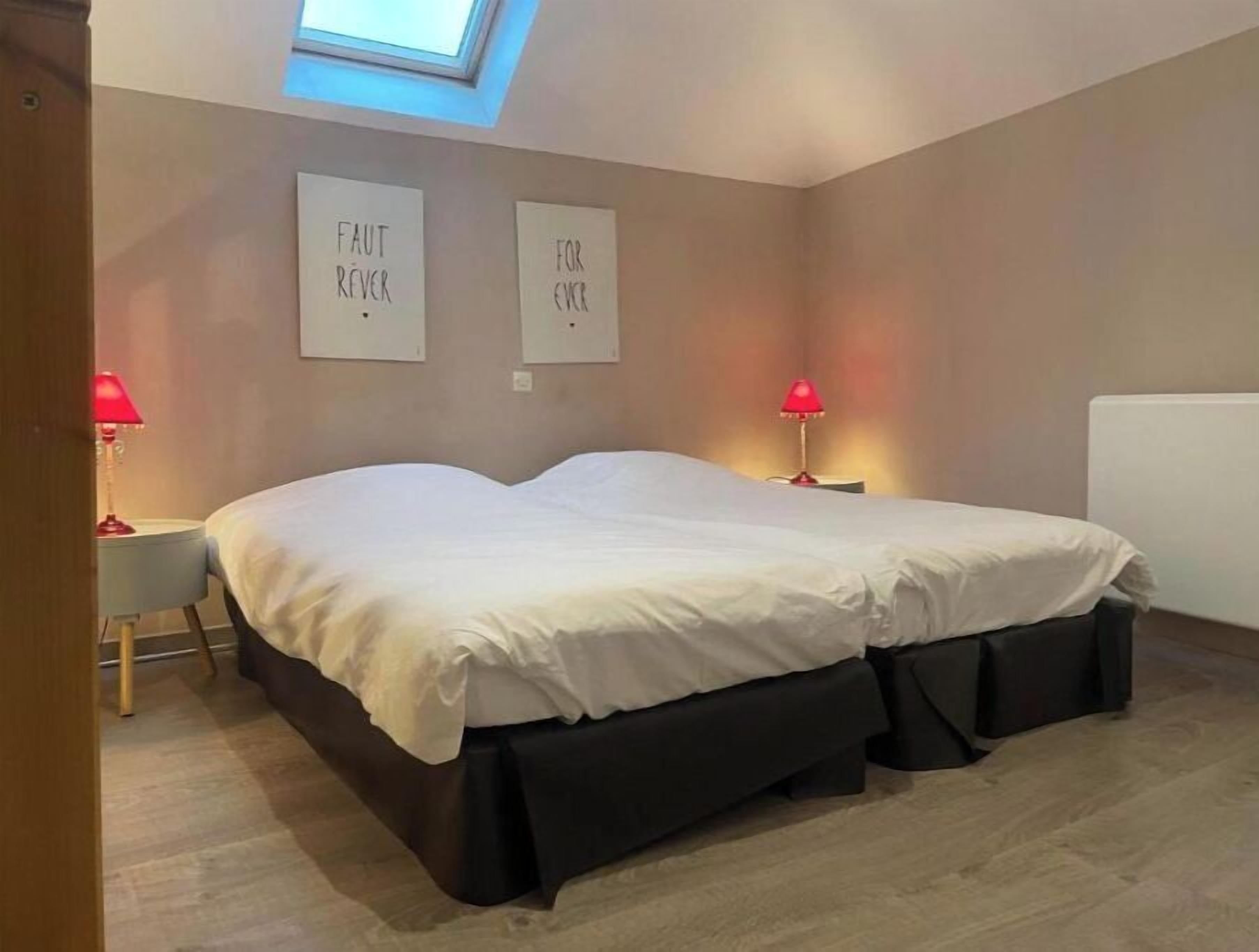 A bedroom with a skylight, two bedside tables with lamps, a bed with white bedding, and two wall-mounted signs.