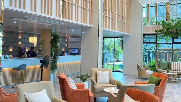 Eine geräumige Lobby mit modernen Möbeln, einer Rezeption und großen Fenstern mit Blick auf Grünflächen.