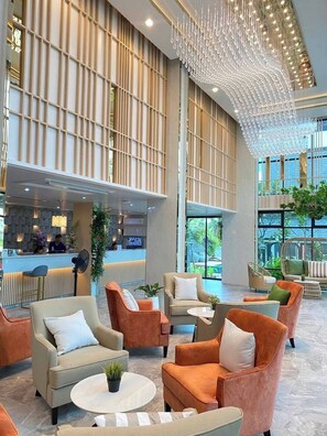 Un hall d’entrée spacieux, doté de meubles modernes, d’un comptoir de réception et de grandes fenêtres offrant une vue sur la verdure.