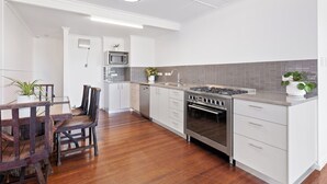 Una cocina moderna con armarios blancos, estufa de acero inoxidable y mesa de comedor de madera con sillas.
