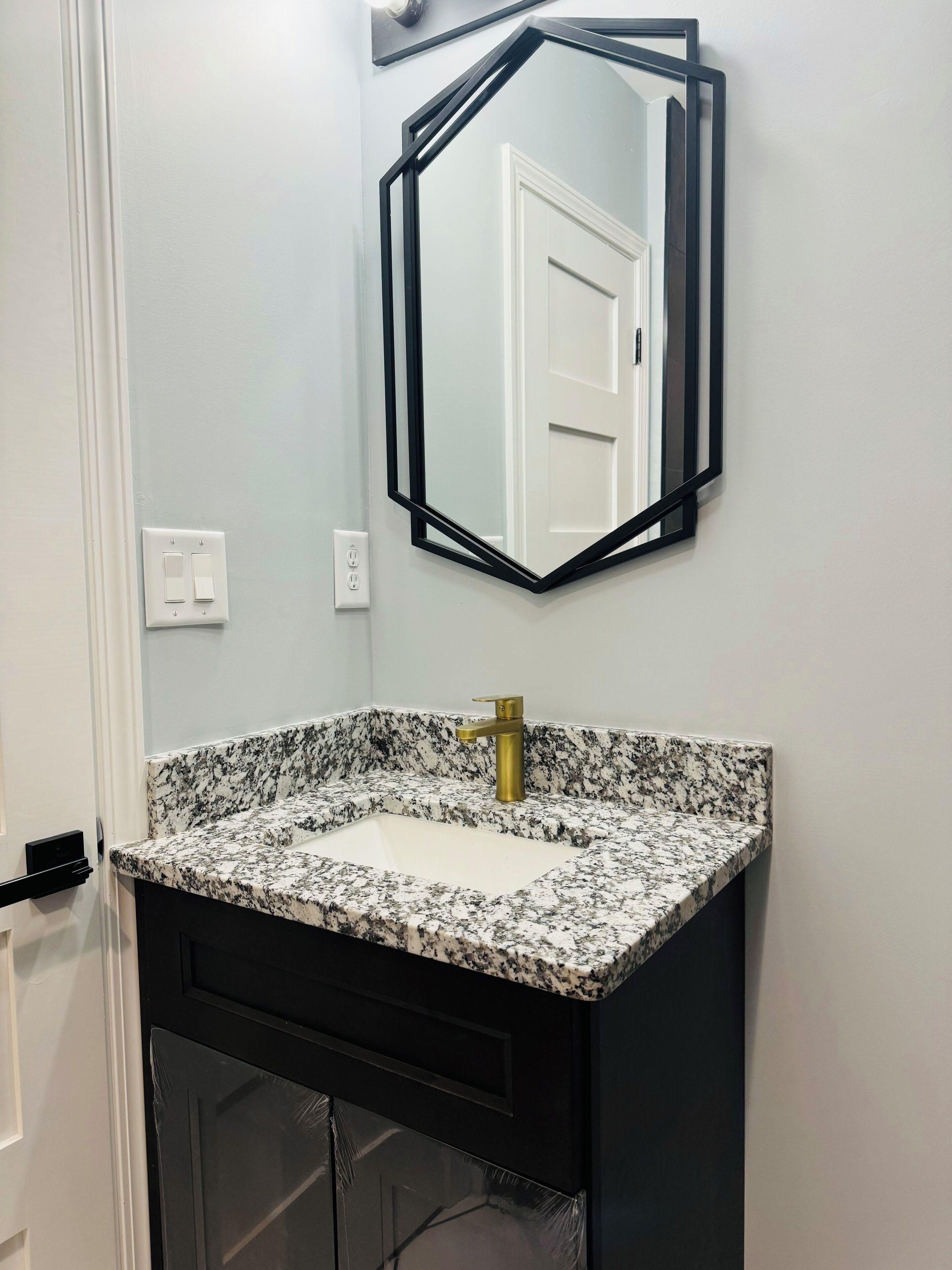 Une salle de bain avec un lavabo à vasque en granit, un robinet doré et un miroir à cadre noir placé au-dessus.