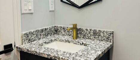 A bathroom with a granite countertop sink, a gold faucet, and a black-framed mirror above it.