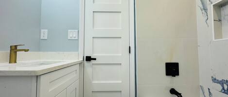 A bathroom with a white door, a sink with a gold faucet, a bathtub, and marble-patterned walls.