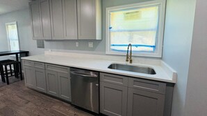 A kitchen with grey cabinets, a stainless steel dishwasher, and a window with a view of a building.