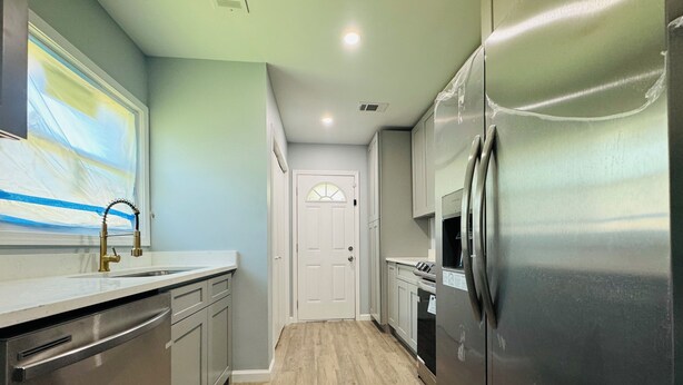 A modern kitchen with stainless steel appliances, a wooden floor, and light blue walls.