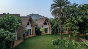 A resort with three treehouse-style cabins, each with a pitched roof and wooden exterior. The cabins are surrounded by lush greenery and a well-maintained lawn. - Ananta Spa & Resort Ajabgarh (Thanagazi)