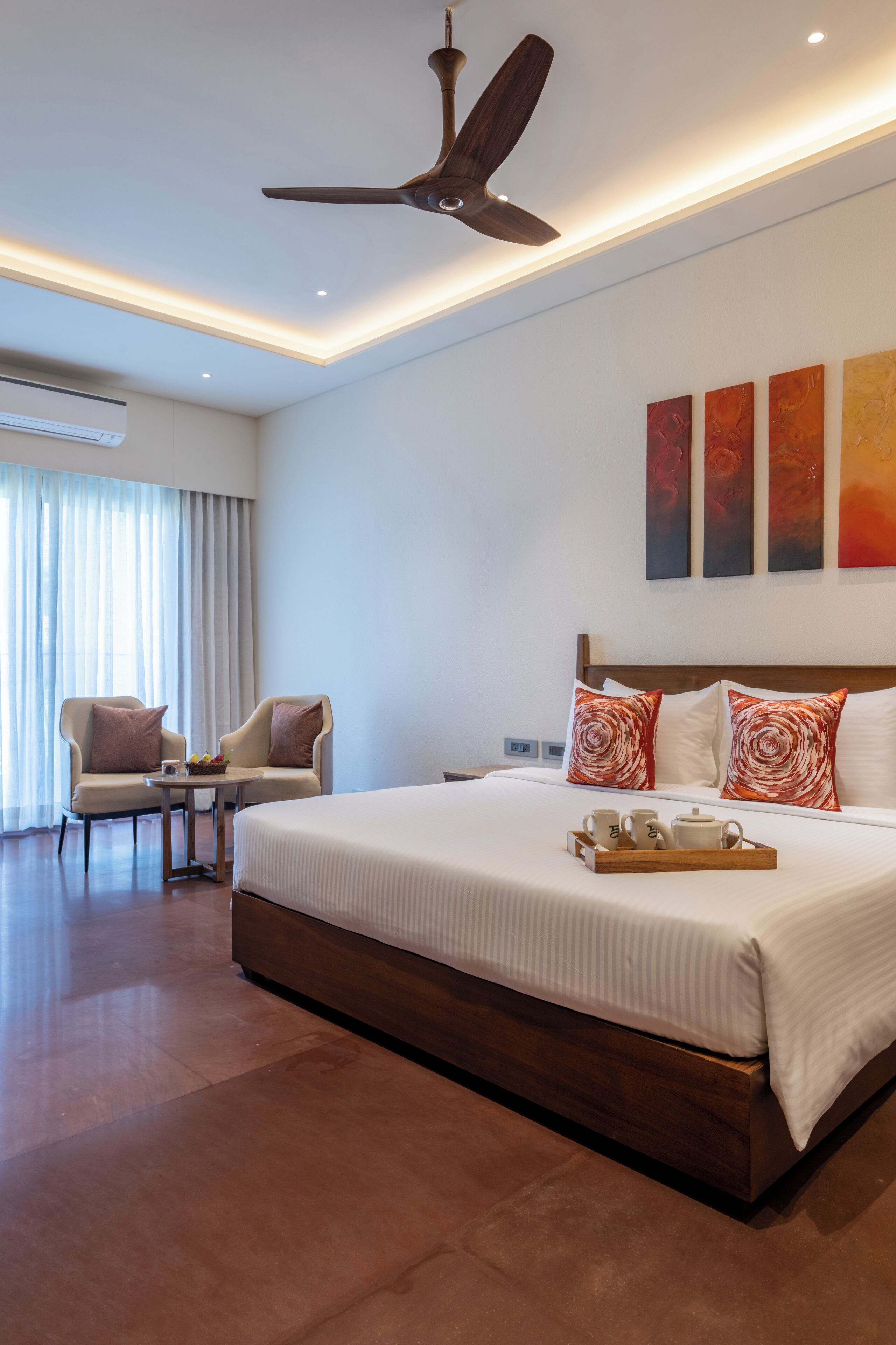 Ein modernes Hotelzimmer mit einem großen Bett, einem Deckenventilator, einem kleinen Tisch mit einer Auflage und einem Stuhl.