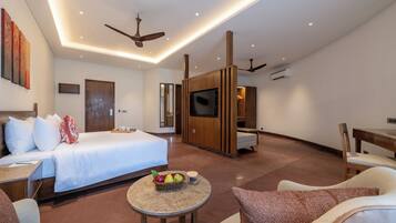 A modern hotel room with a bed, seating area, TV, and a small table with fruit.