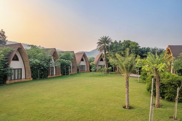 A row of bungalow-style accommodations with pitched roofs, surrounded by a well-maintained lawn and various tropical plants.