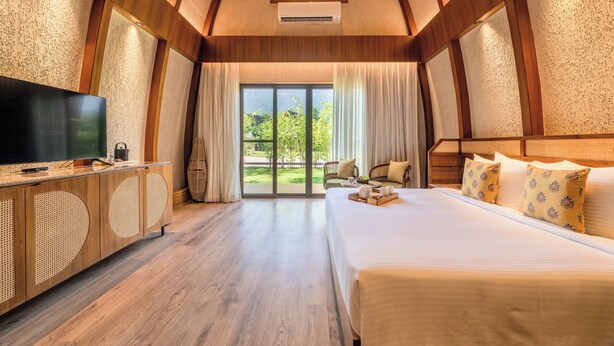 A bedroom with a large bed, a television, and a view of greenery through a sliding glass door. - Ananta Spa & Resort Ajabgarh (Thanagazi)