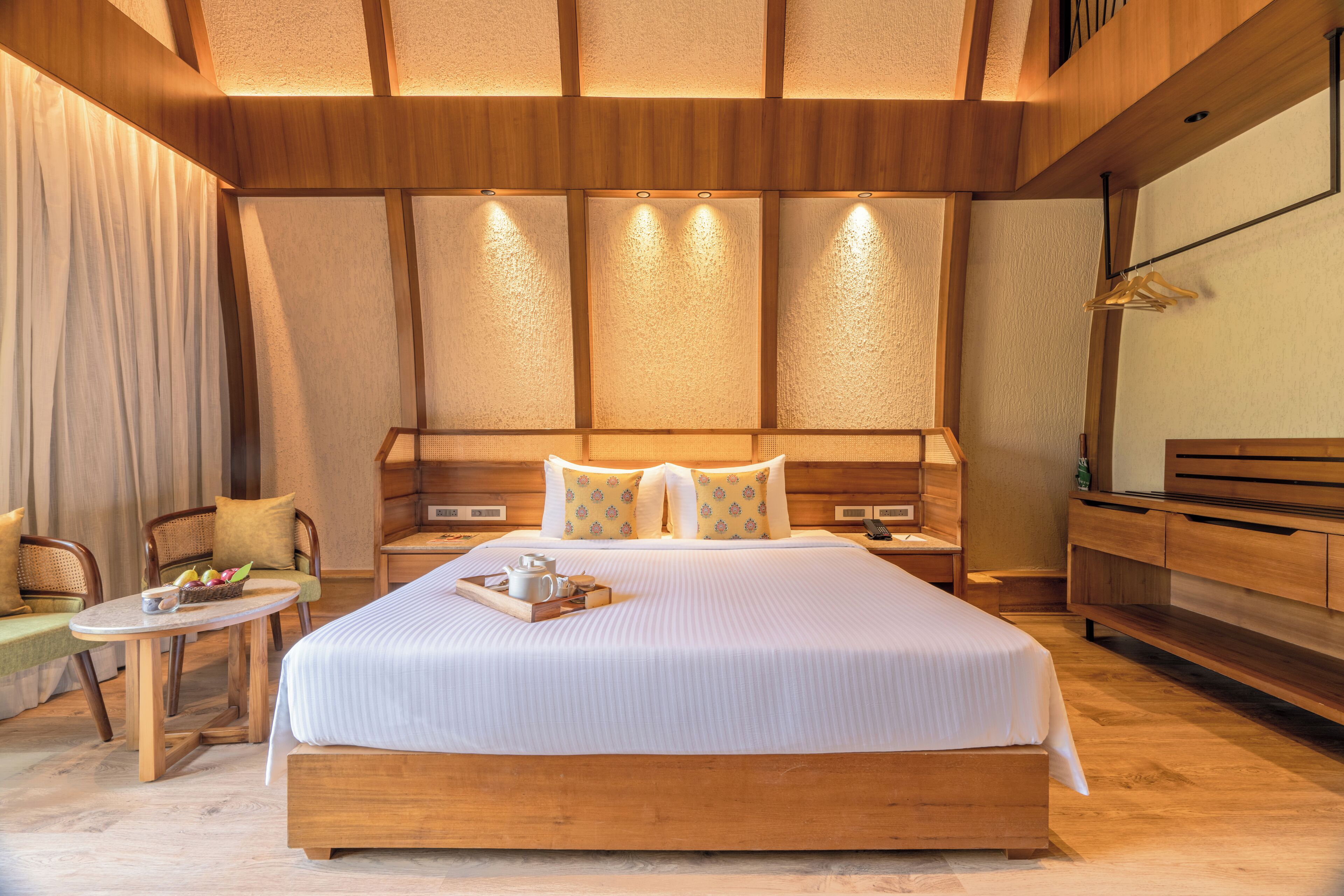 A hotel room with a large bed, wooden headboard, bedside tables, a small round table with a tray, and a chair.