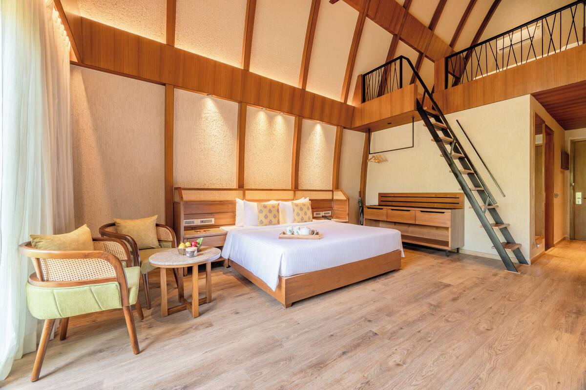 A spacious bedroom with a large bed, wooden furniture, a small table, and a staircase.