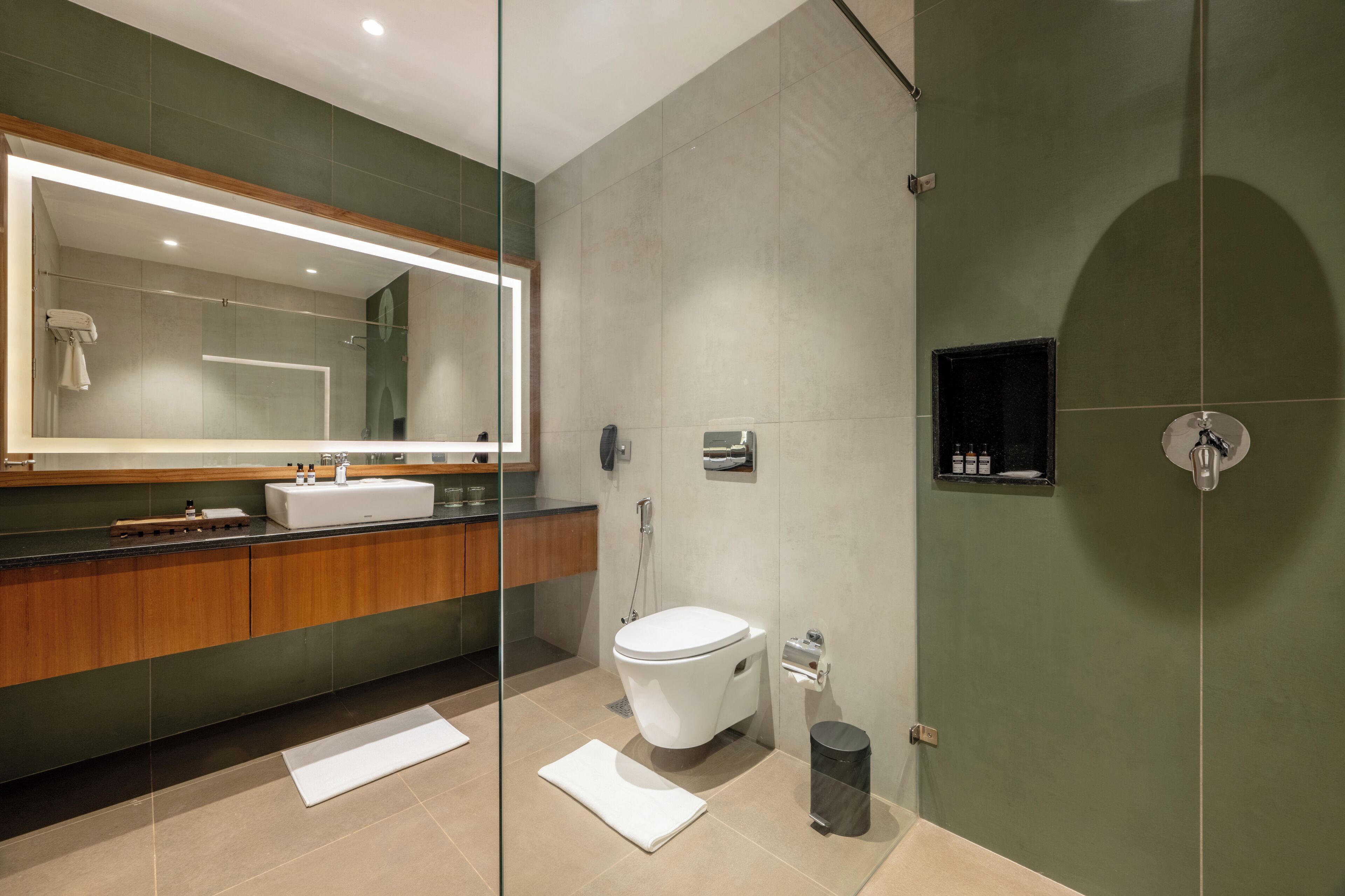 A modern bathroom with a glass shower enclosure, a large mirror, a wooden vanity, and a toilet.