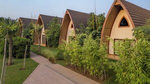 A row of modern, arched-roofed cottages with a pathway leading through a lush garden. - Ananta Spa & Resort Ajabgarh (Thanagazi)