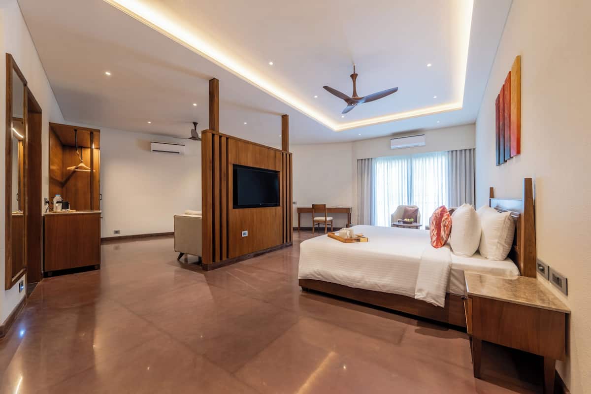 A modern hotel room with a large bed, a flat-screen TV, a desk, and a ceiling fan.