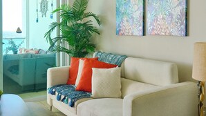 Un salón con sofá, una mesita de centro, una planta en maceta y obras de arte en la pared.