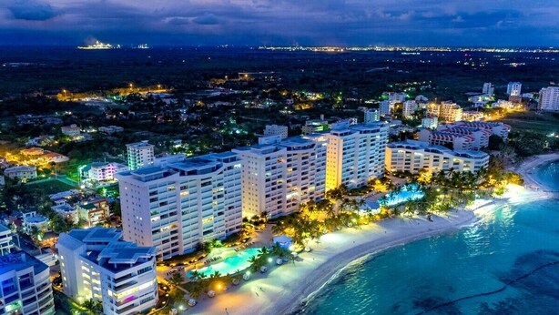 Un hotel costero con varios edificios altos, una playa y una piscina.