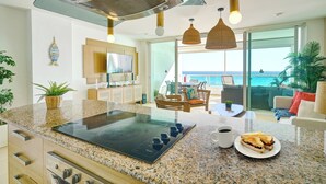Una cocina con placa de inducción, un comedor con vista al océano y un espacio de estar con una mesa y sillas.
