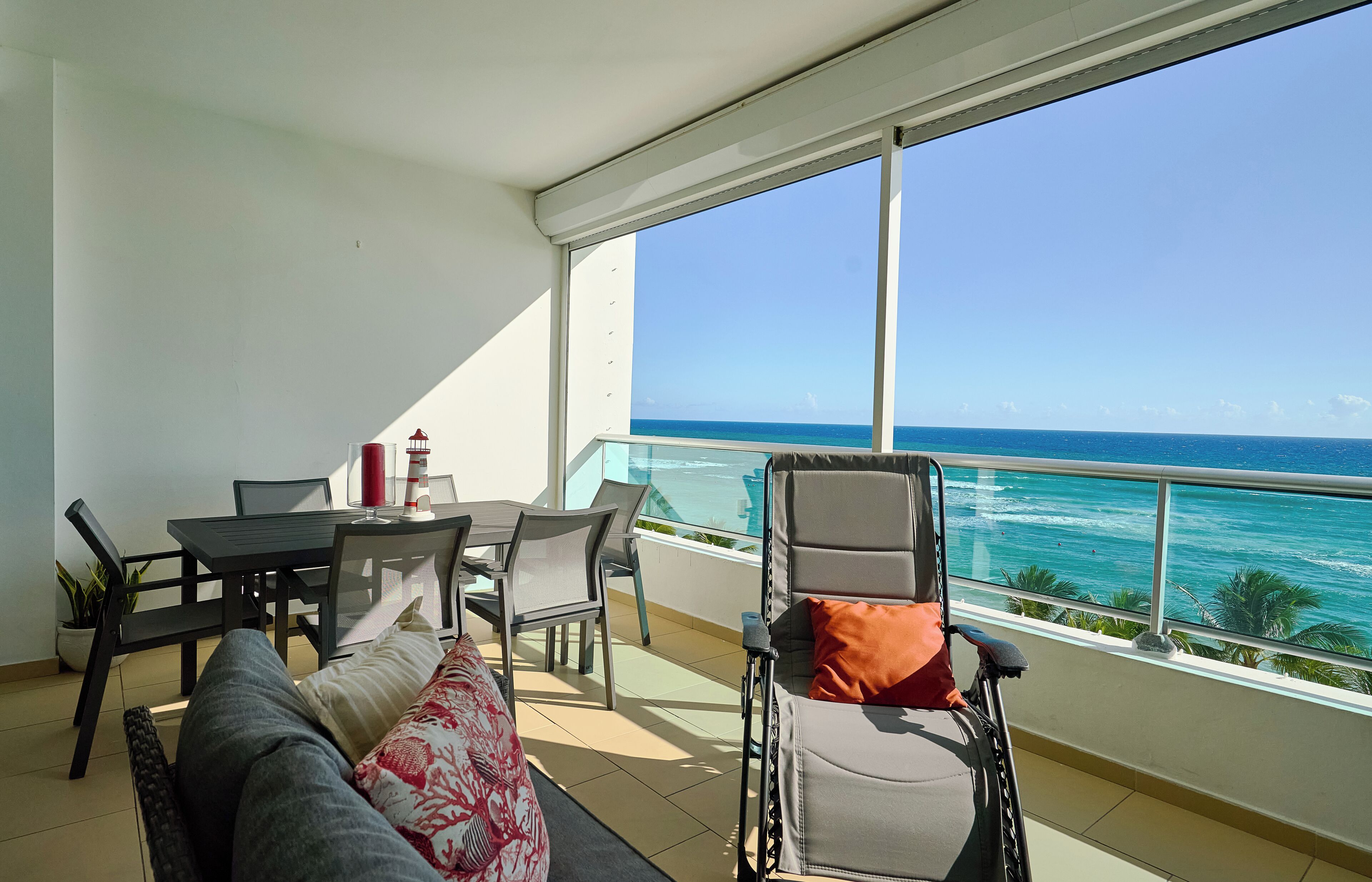 Een balkon met uitzicht op de oceaan, een rolstoel, een eettafel met stoelen en een bank.