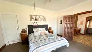 Un dormitorio con cama, mesitas de noche, una lámpara colgante, una puerta y una alfombra estampada.