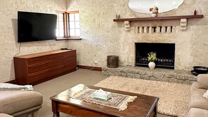 Sala de estar con televisor de pantalla plana, chimenea, mesa de centro de madera y sofás color beige.