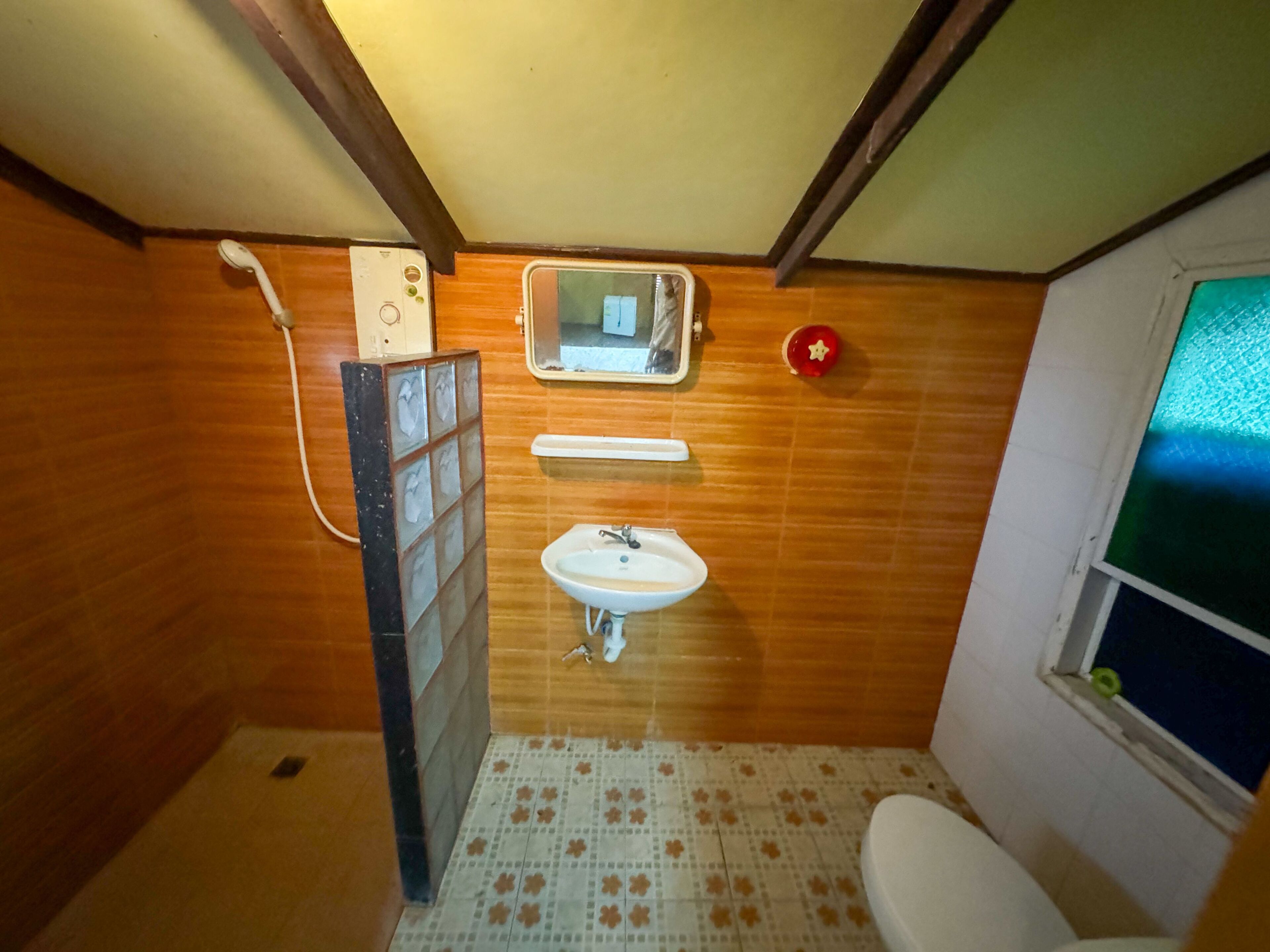A small bathroom with a wooden floor, a white sink, a mirror above the sink, and a toilet.