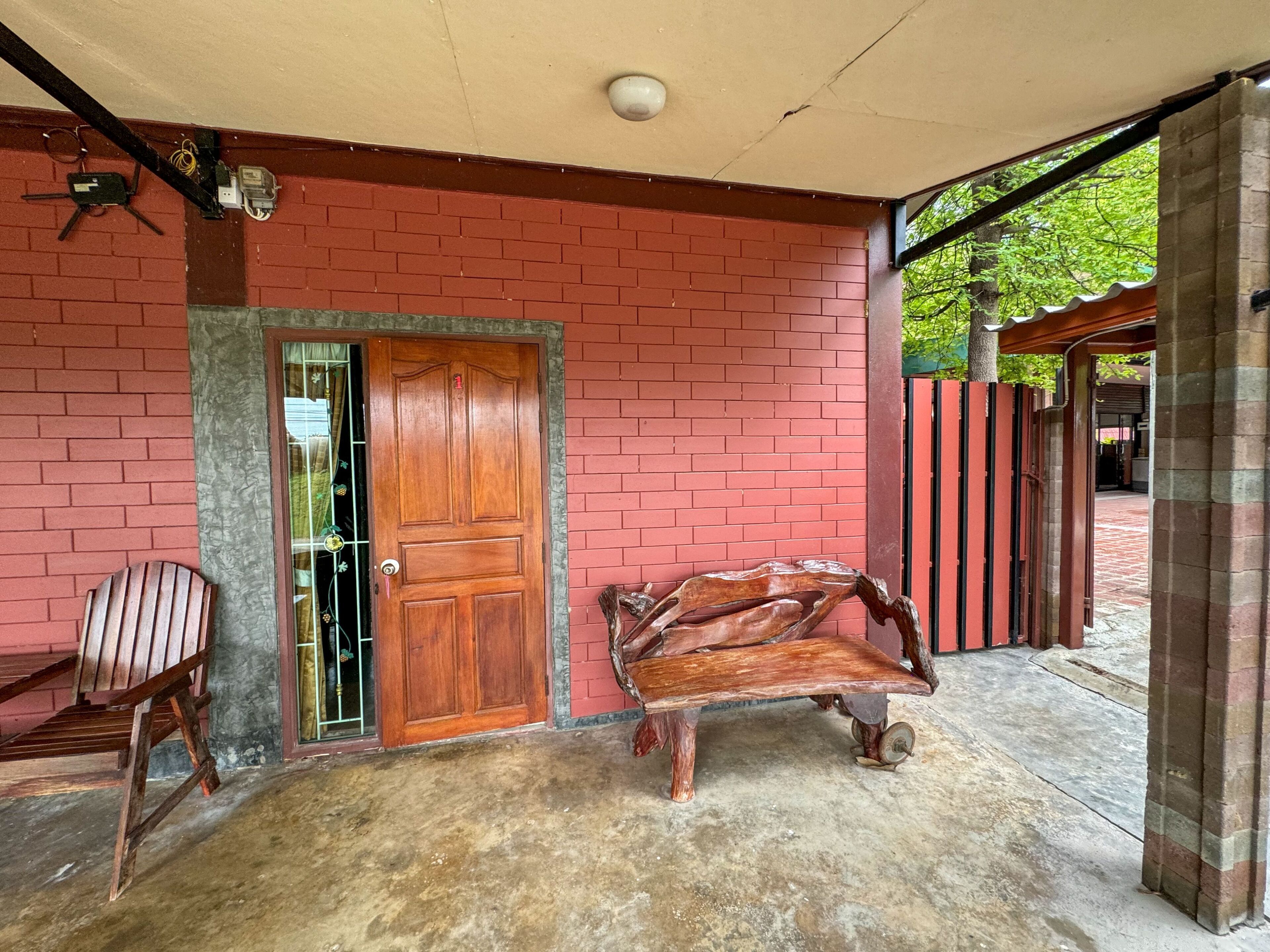 Un porche cubierto con un muro de ladrillo rojo, una puerta de madera, un banco y una silla.