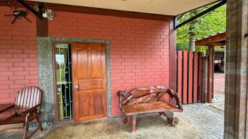 Un porche cubierto con un muro de ladrillo rojo, una puerta de madera, un banco y una silla.