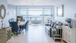 Ein großzügiger Wohnbereich mit Meerblick, ein Essbereich mit Tisch und Stühlen sowie eine Sitzecke mit Sofa und Kissen.