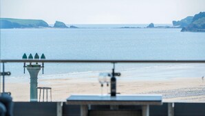Blick auf einen Strand mit einer Geländer, einem Lampenpfahl und in der Ferne Klippen.