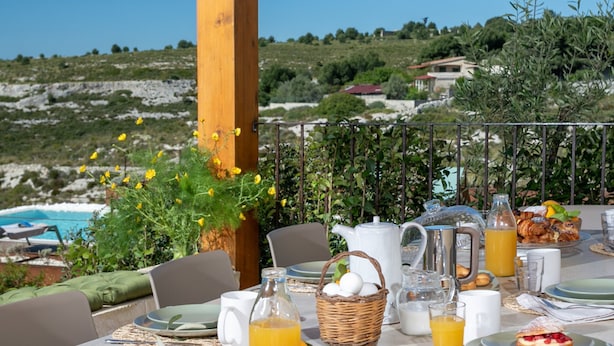 Ein Tisch ist für ein Frühstück gedeckt, mit Blick auf das Meer und die Hügel.
