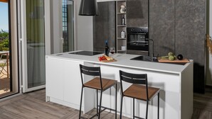 Eine moderne Küche mit einer zentralen Kochinsel, zwei Barhocker, einem Einbauofen und einer Glastür zum Außenbereich.