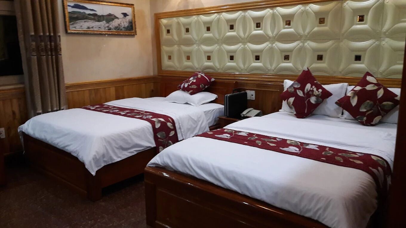 Two double beds with white and red floral bedspreads, a wooden headboard, and a painting on the wall.
