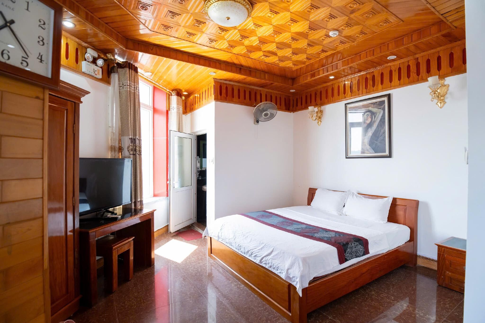 Ein Hotelzimmer mit Holzbalkendecke, einem Bett mit weißen Leinen, einem Fernseher auf einem Holztischchen und einer Uhr an der Wand.
