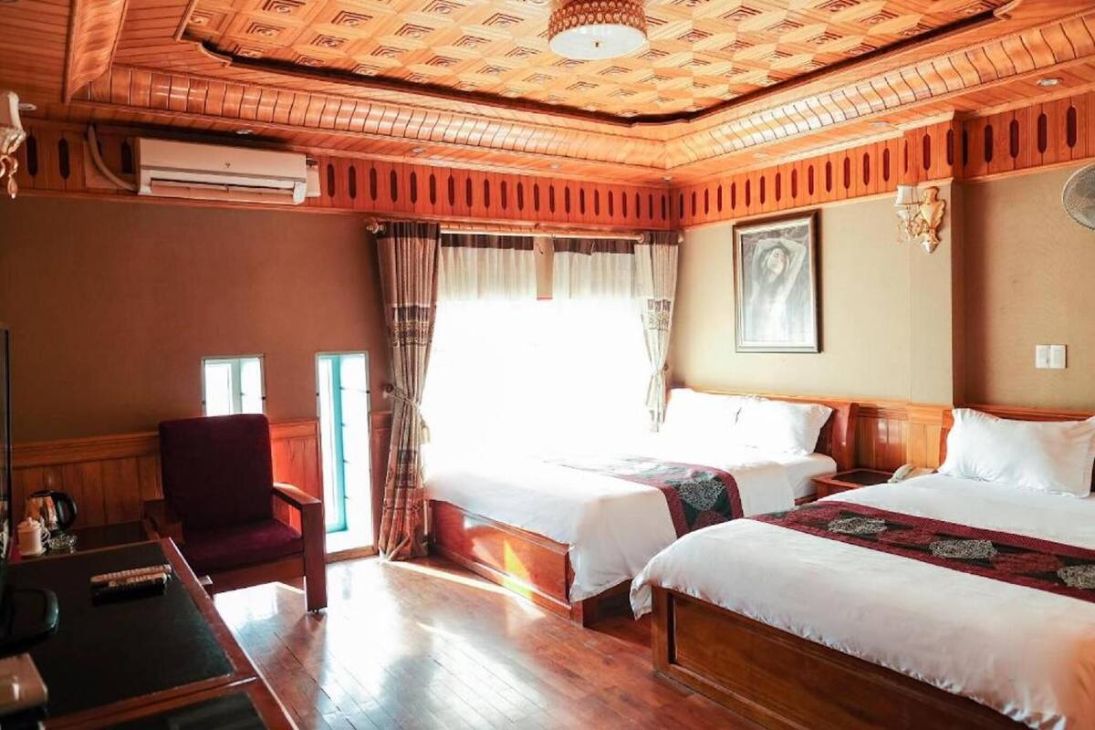 Une chambre d’hôtel avec deux lits, un bureau, une chaise et une grande fenêtre avec des rideaux.