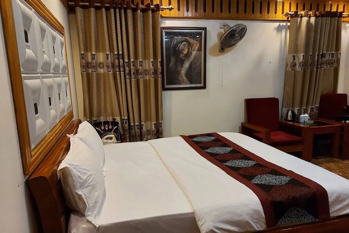 Une chambre d’hôtel avec un lit, un bureau, une chaise, un ventilateur et des rideaux.