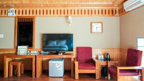 A cozy room with a wooden ceiling, a flat-screen TV, a desk with a computer, two red chairs, and a small refrigerator.