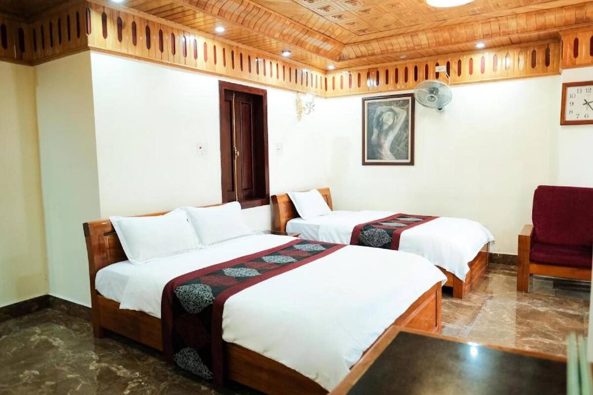 Une chambre d’hôtel avec deux lits en bois, une chaise rouge, une horloge et un tableau accroché au mur.