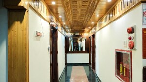 A corridor with a polished floor, wooden ceiling with recessed lighting, and a fire extinguisher mounted on the wall.