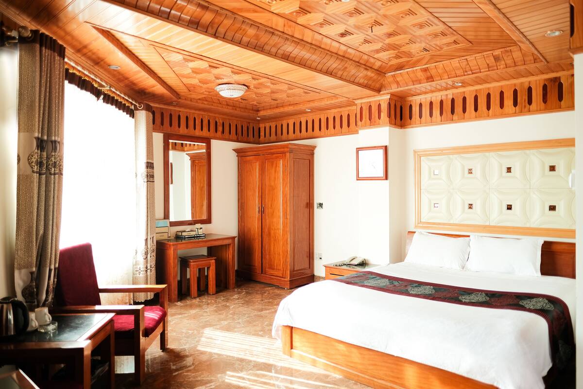 Une chambre d’hôtel avec un plafond en bois, un grand lit, un bureau avec une chaise, une armoire et un miroir.