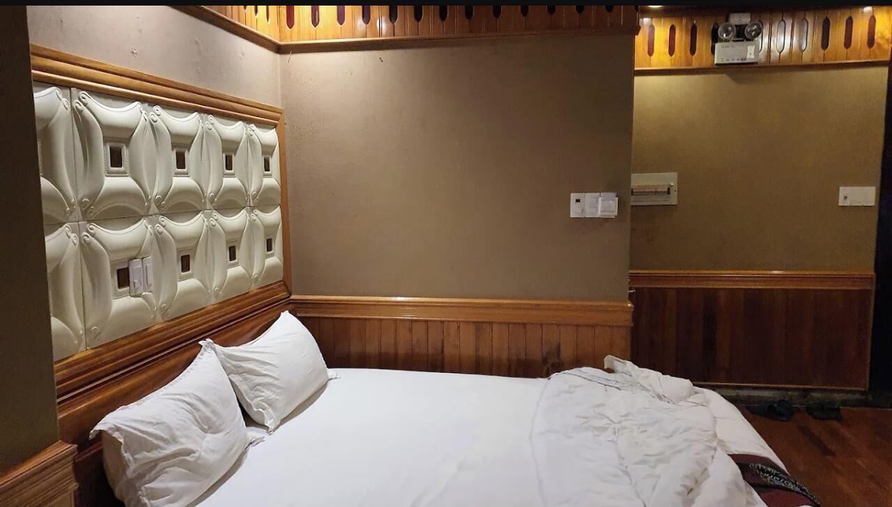 A hotel room with a wooden headboard, a bed with white linens, and a wooden floor.