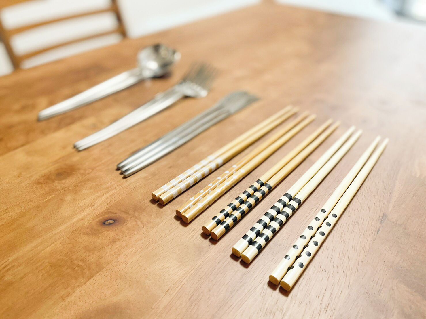 A wooden table with chopsticks, a spoon, and a fork.