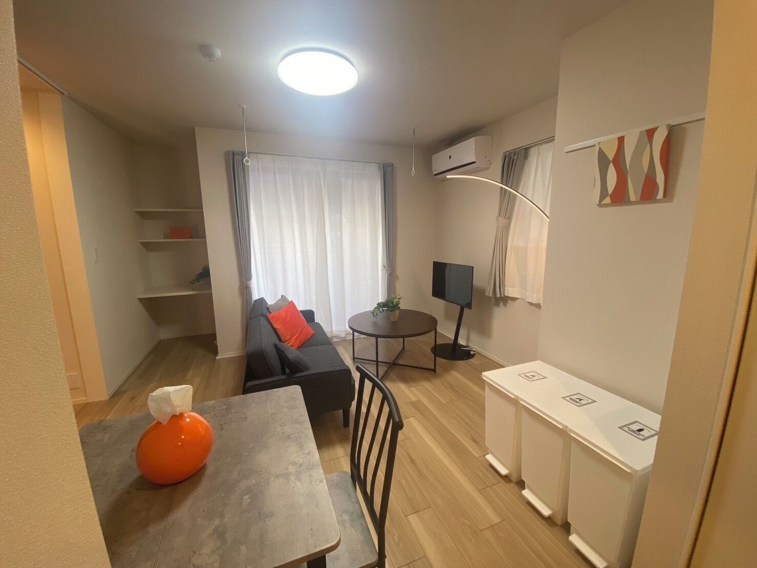 A compact living space with a sofa, a small dining table, a TV, and a kitchenette.