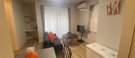 A compact living space with a sofa, a small dining table, a TV, and a kitchenette.