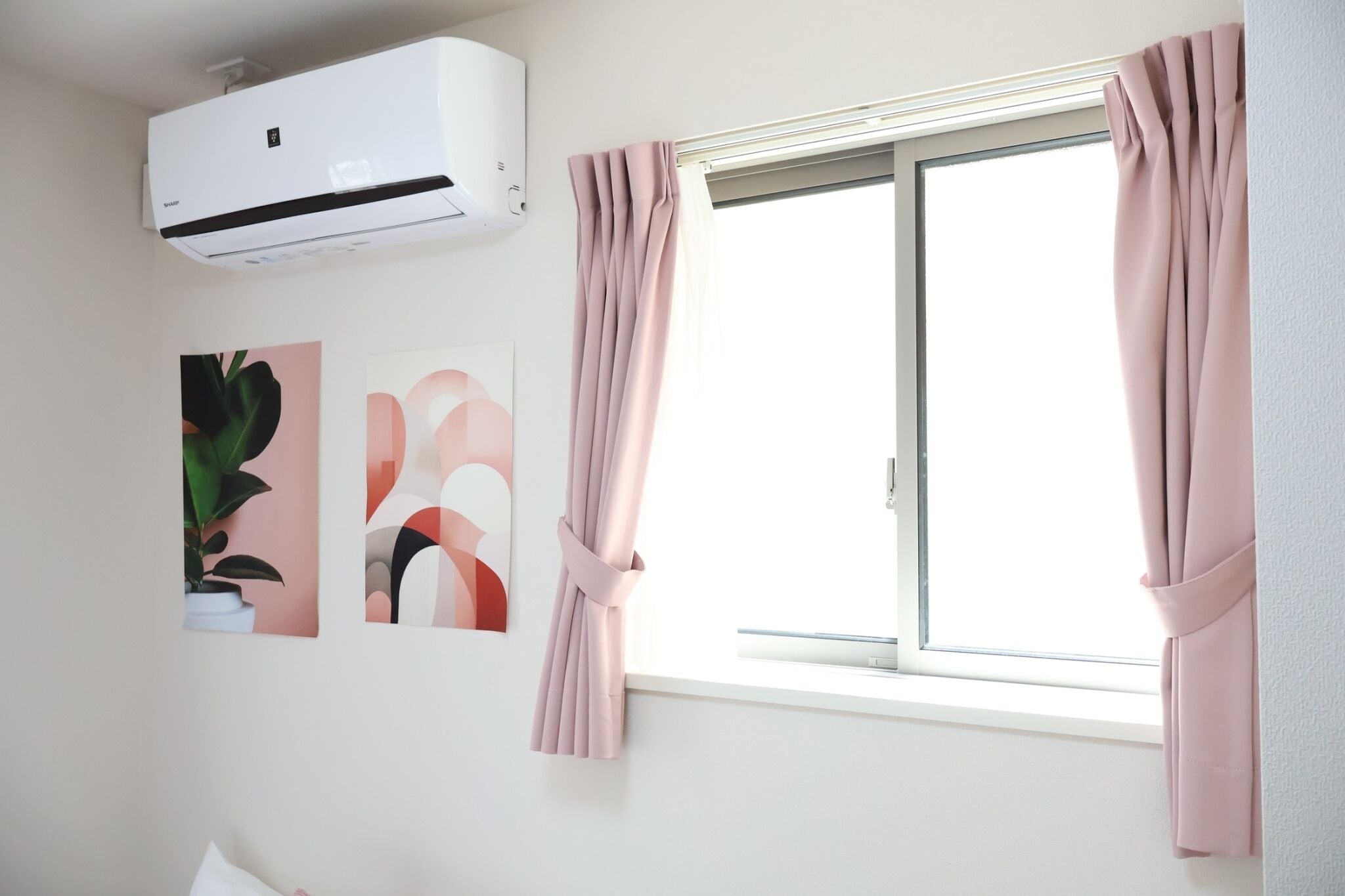 A room with a window, pink curtains, an air conditioner, and two abstract wall art pieces.