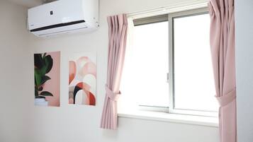 A room with a window, pink curtains, an air conditioner, and two abstract wall art pieces.