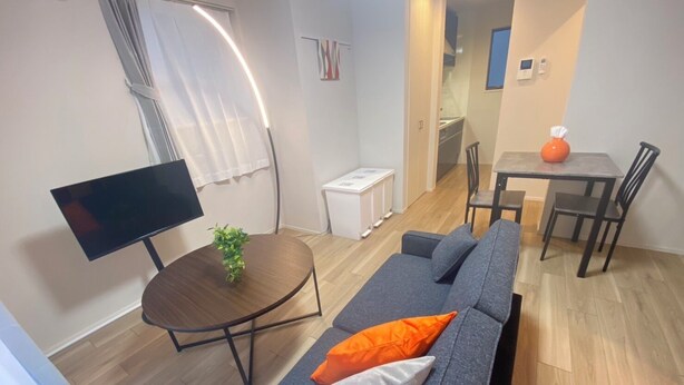 Ein modernes Wohnzimmer mit einer Couch, einem kleinen runden Tisch, einem Flachbildfernseher und einem Essbereich mit Tisch und Stühlen.