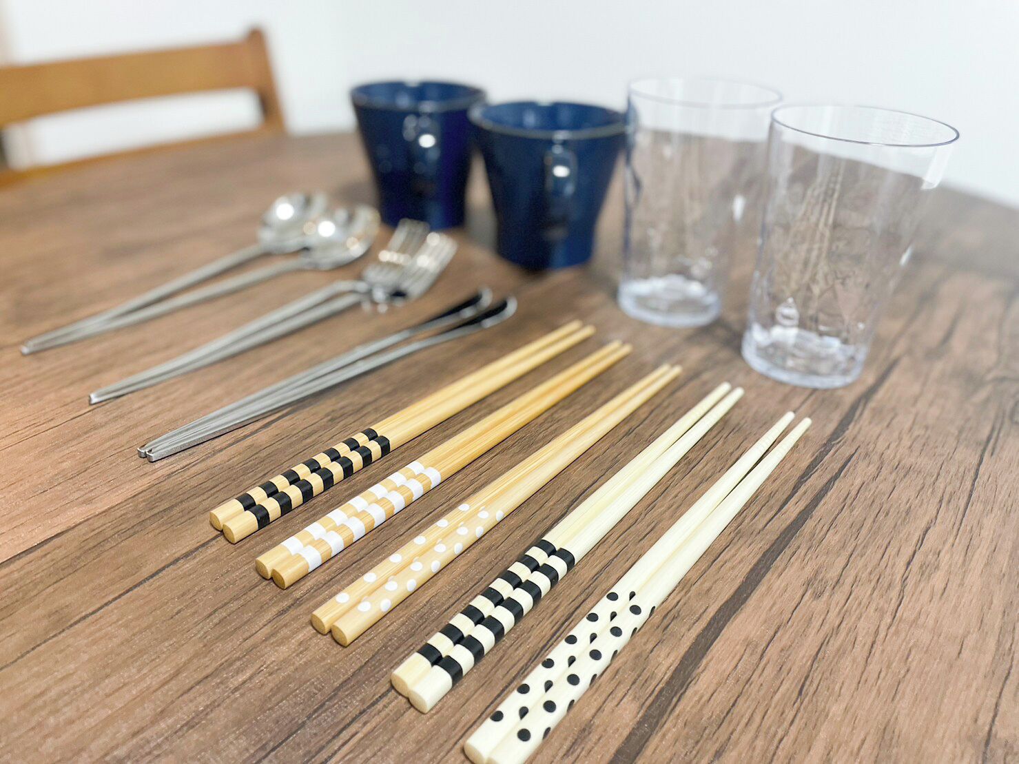 Una mesa de madera con palillos, cucharas y vasos.