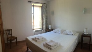 Ein Schlafzimmer mit einem großen Bett, einem Sessel, einem Nachttisch, einer Lampe, einem Fenster mit Vorhängen und einer Heizung.